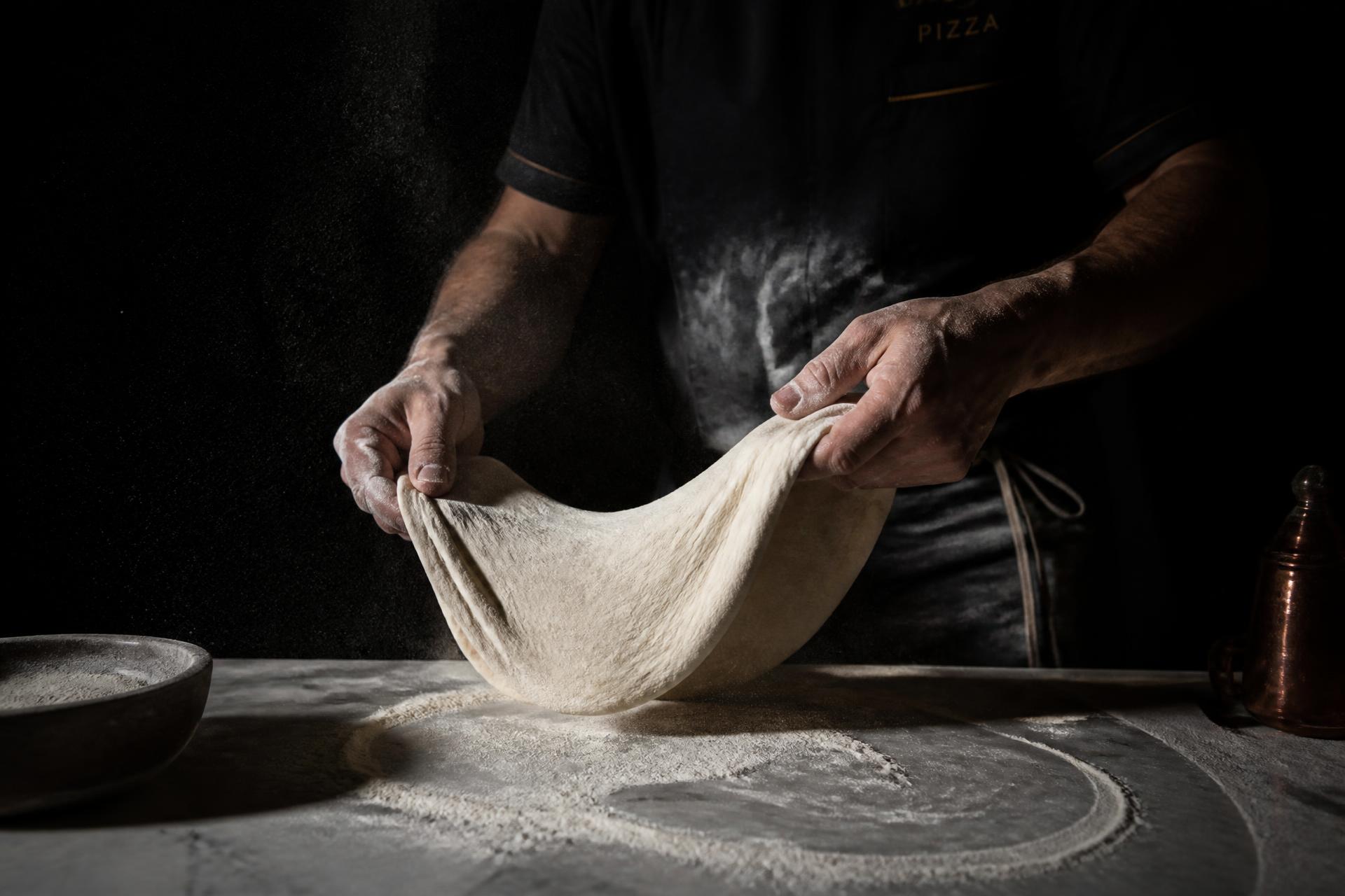 Pizzaiolo abrindo uma massa de alta hidratação sobre bancada de mármore